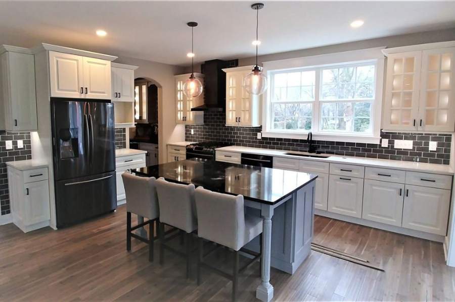 21st Century Avalon white kitchen with a black island, glass uppers and pendant lights — manufacturer photo