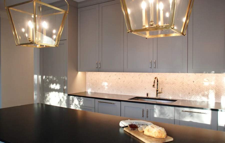 Great Northern slab-door kitchen with a black countertop and brass pendants — manufacturer photo