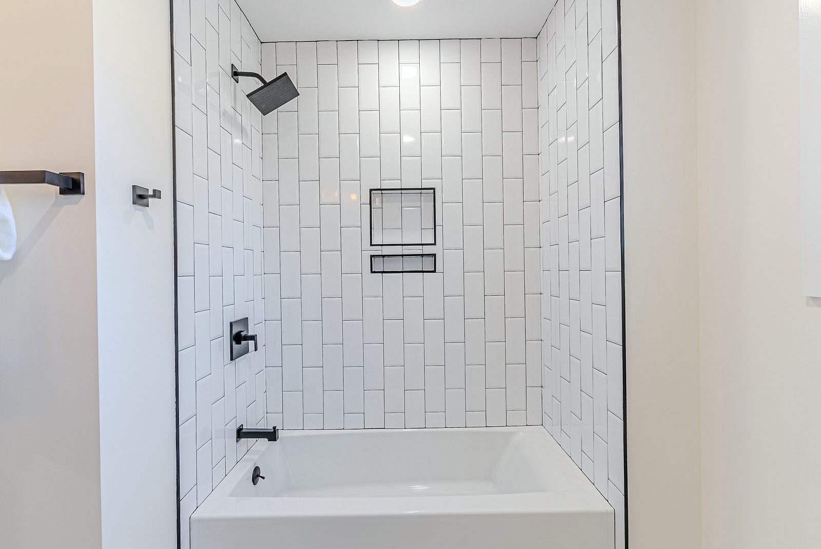 Tub-shower in vertically stacked white subway tile — White-oak and navy bathroom vanities with a freestanding tub and black fixtures