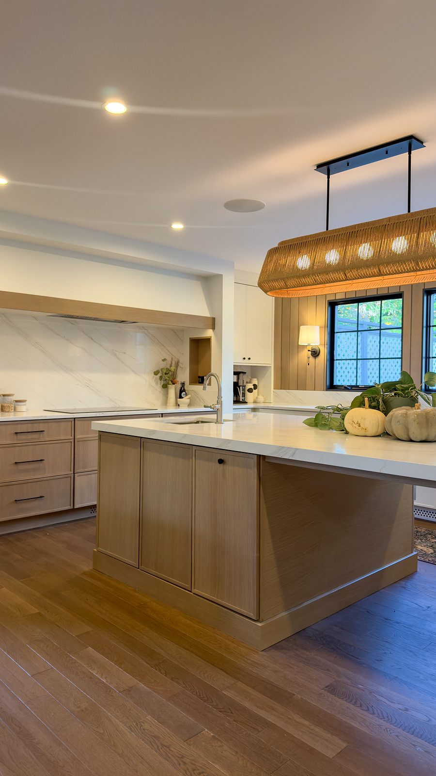The white-oak island with its table-height extension under the rattan pendant