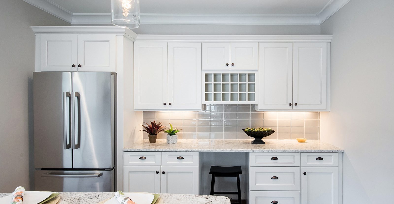 Lantern pendants, wine-cubby cabinet — Fabuwood Fusion in Blanc with a granite island and an arched hood