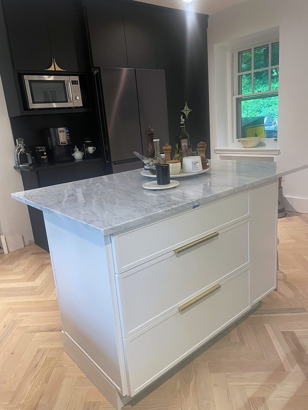 Marble-look slab backsplash under a stainless chimney hood — Fabuwood Luna kitchen in matte black with a Dove island and a herringbone floor