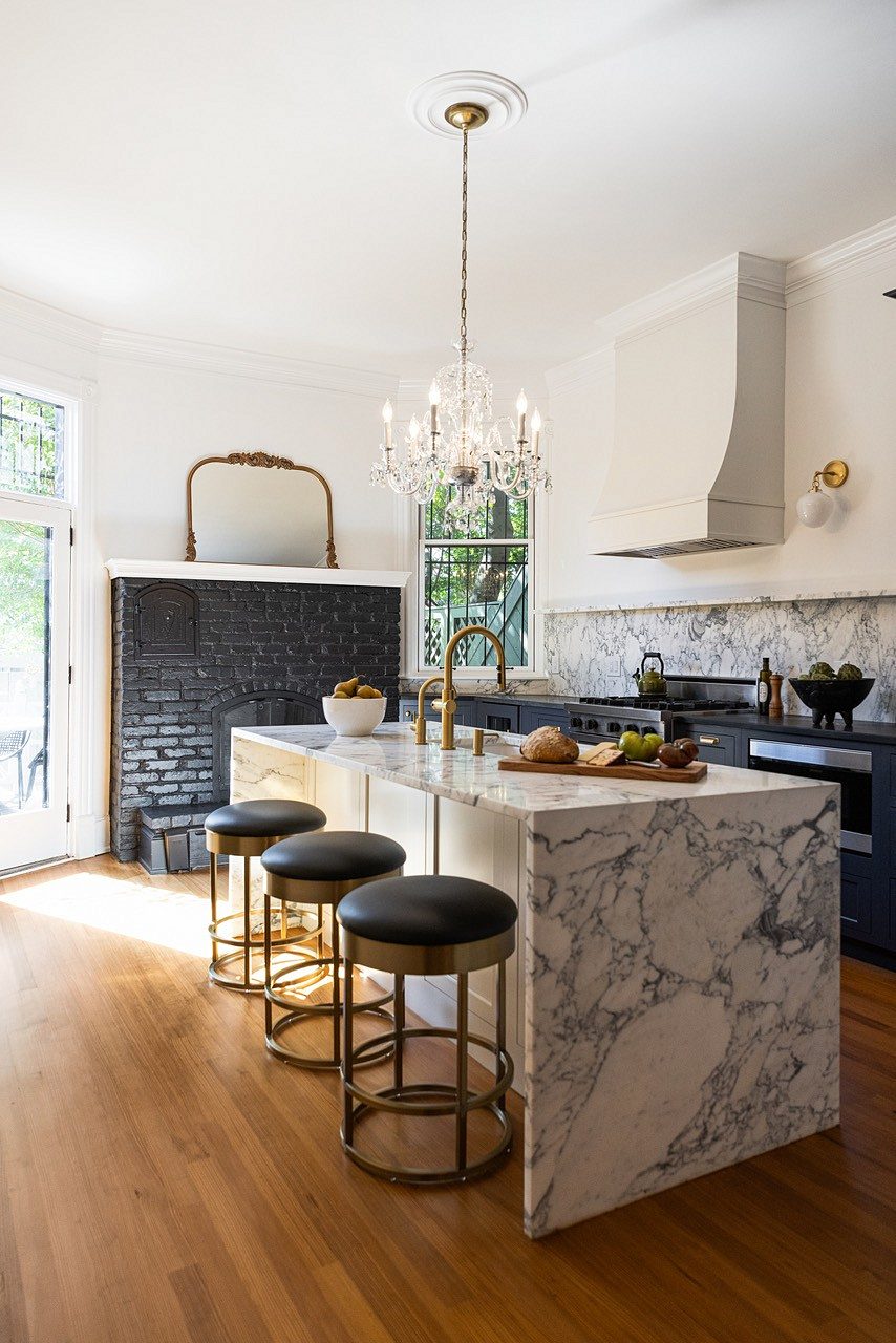 The marble waterfall island with three brass-based leather stools, the plaster hood and chandelier