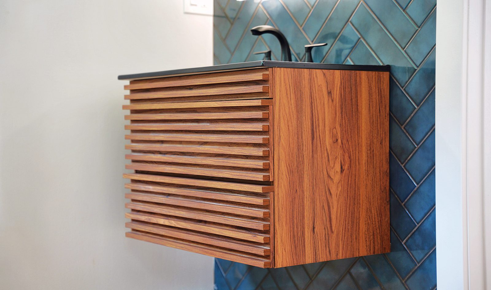 Walnut slat vanity against teal tile