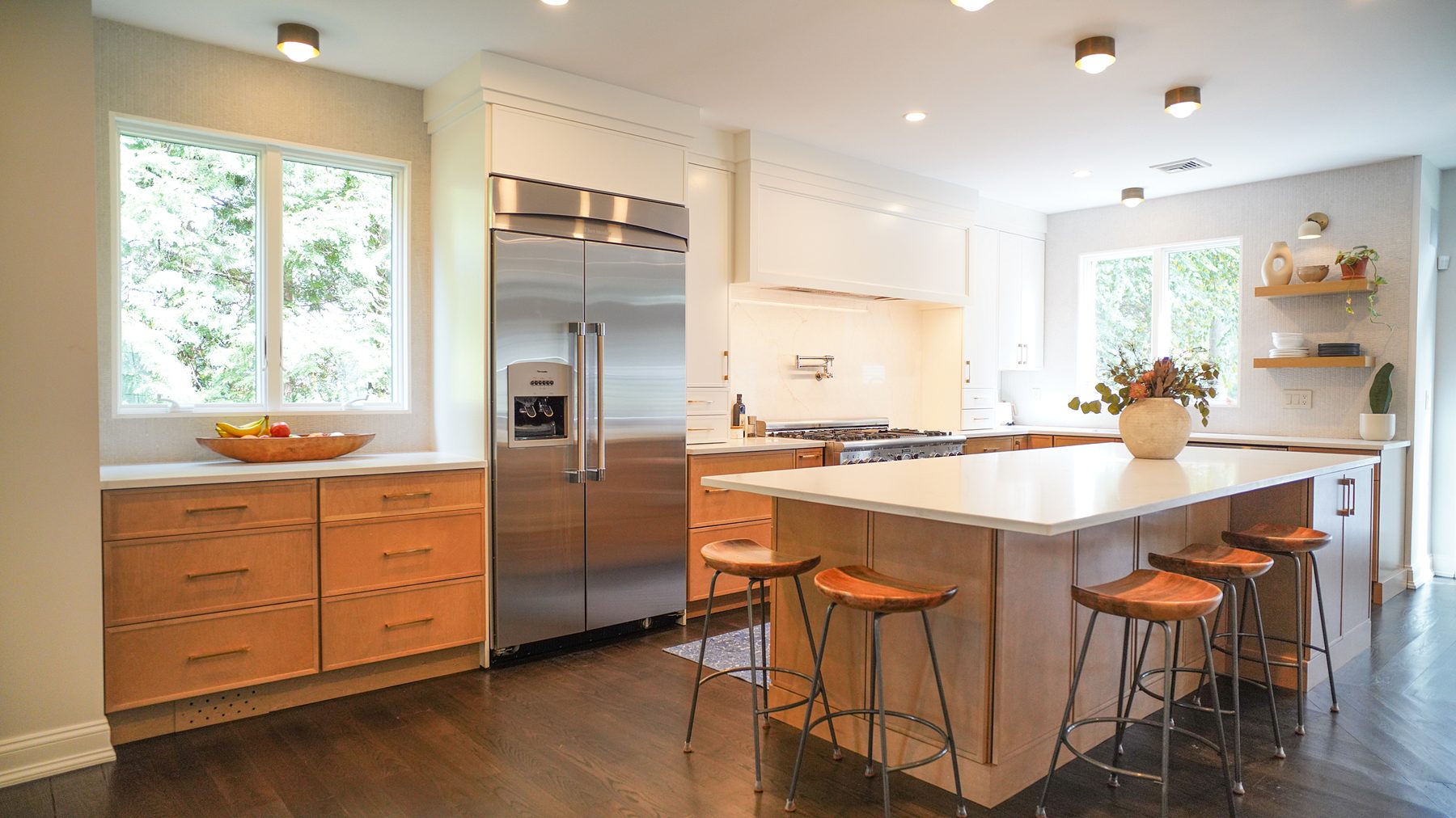 Honey oak and white flat-panel kitchen with a white quartz island, saddle stools and a built-in stainless refrigerator