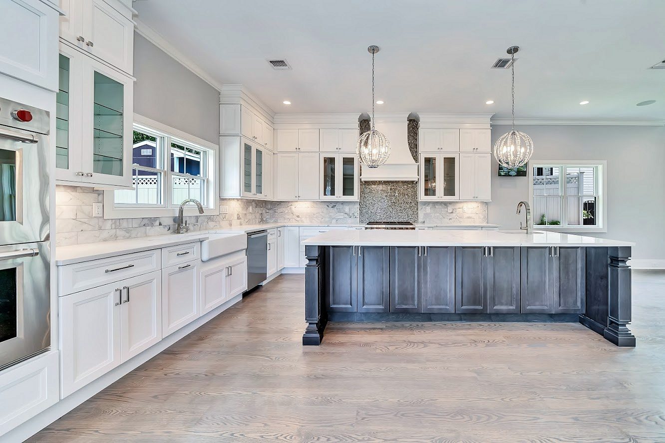 White hood cabinet with a mosaic inset; pro-style range — White shaker kitchen with a long charcoal island in a two-story great room