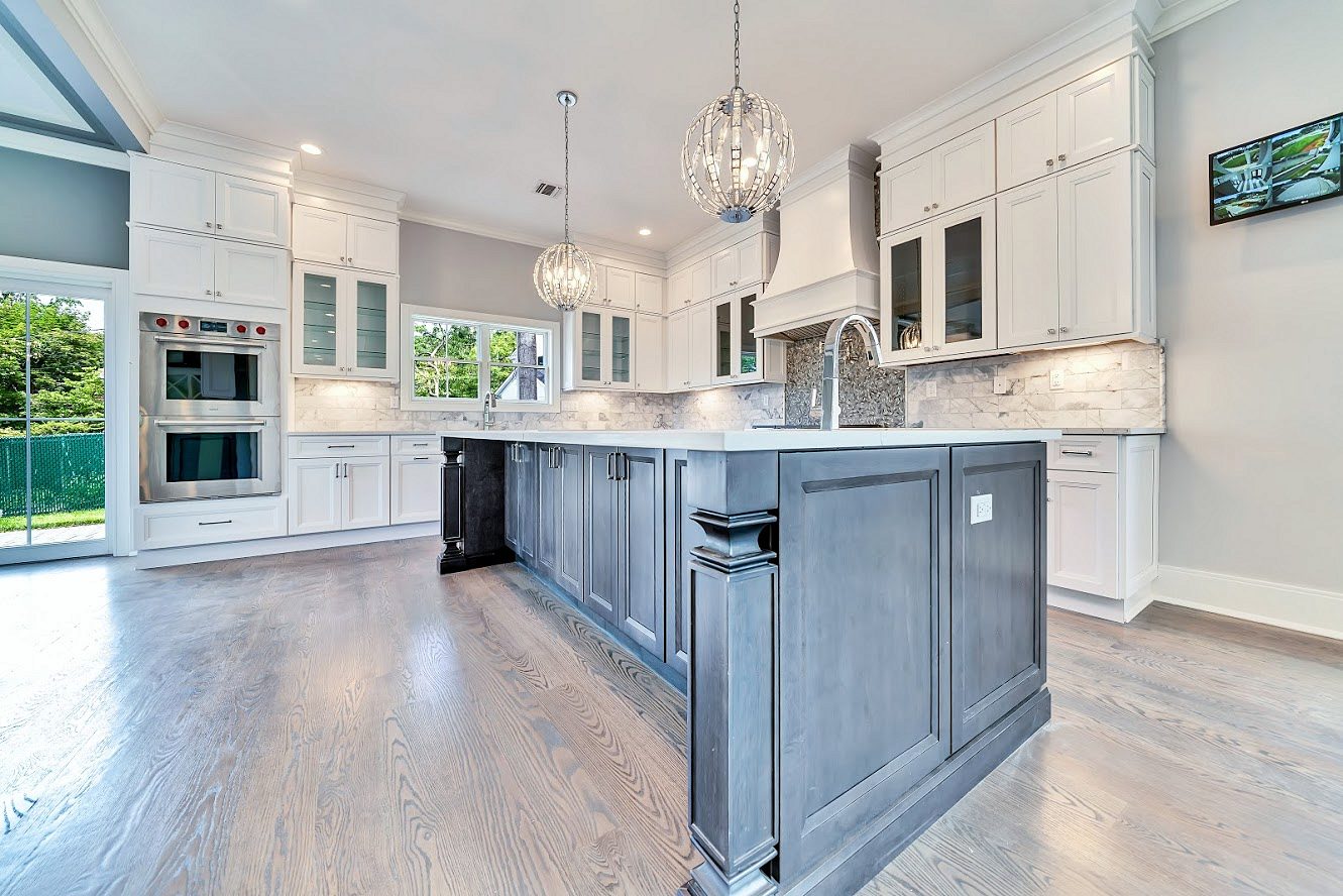 Two-story great room, wide-plank gray-wash oak — White shaker kitchen with a long charcoal island in a two-story great room