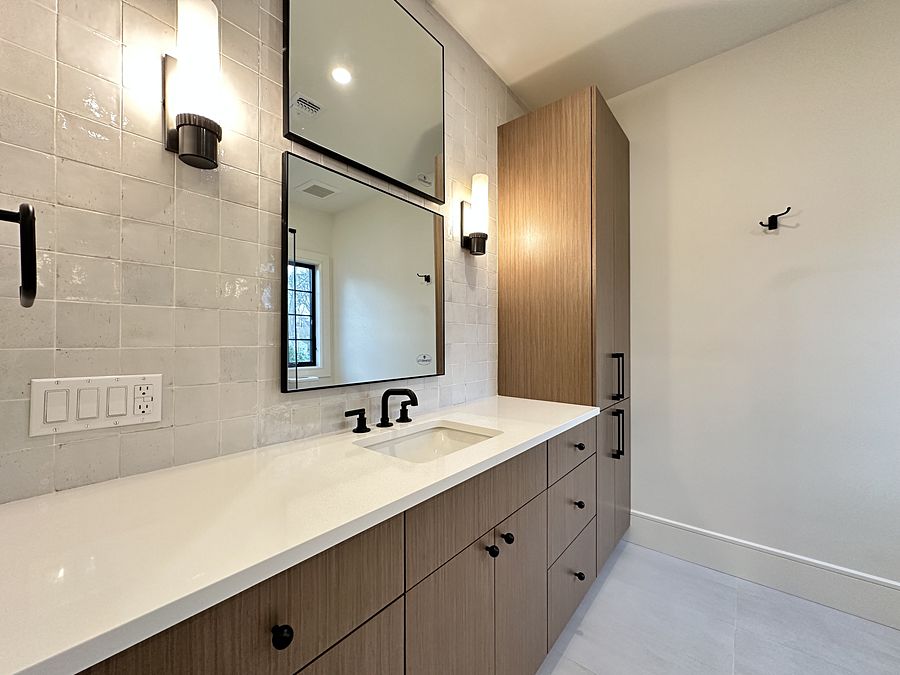Wood-grain slab vanity with a white quartz top, matte black faucet and black-framed mirror against a zellige-look tile wall