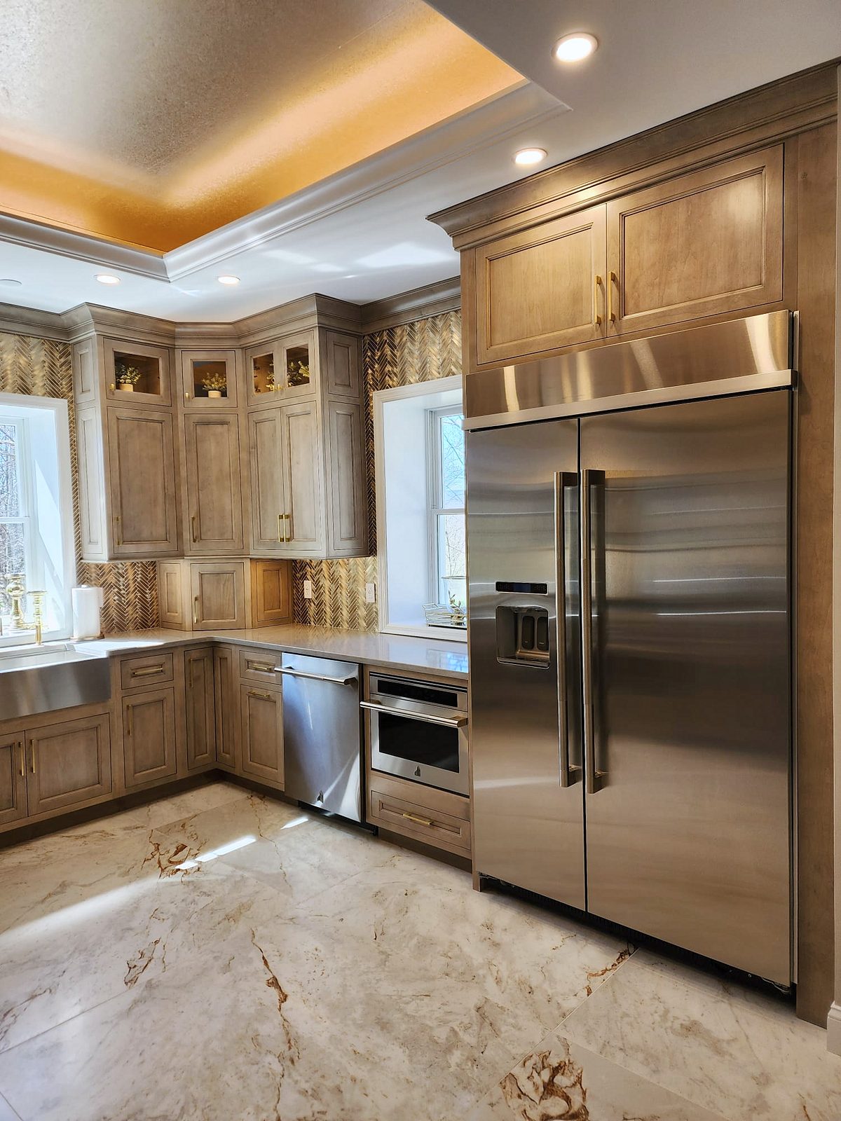 Lit glass-front uppers, bronze herringbone mosaic — Shiloh Aspen inset kitchen in a brown stain with a lit bar wall and a butler’s pantry