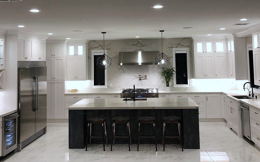Black island with a gray marble-look top and black stools — St. Martin white shaker kitchen with a black island and a marble-look slab backsplash