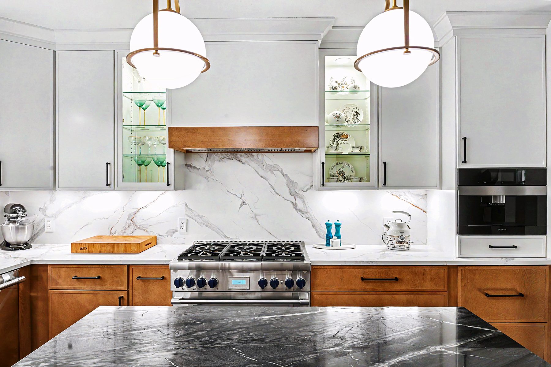 Two-tone kitchen with black marble waterfall island and brass pendants