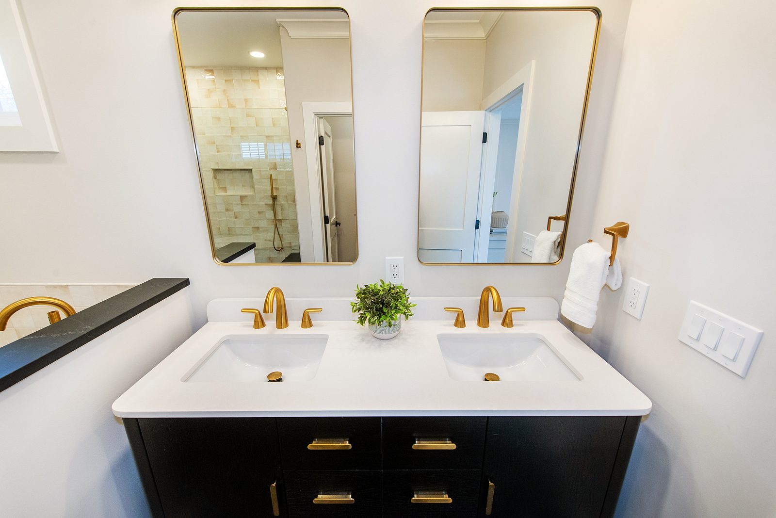 Primary bath: black double vanity with brass pulls under two brass-framed mirrors