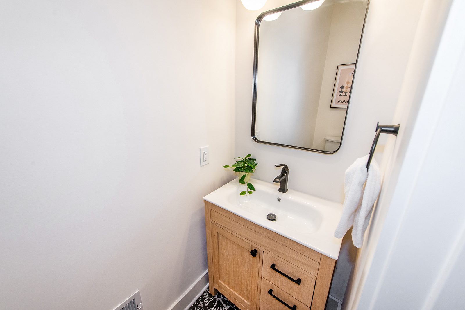 Powder room with a small white-oak vanity, black faucet and black-framed mirror