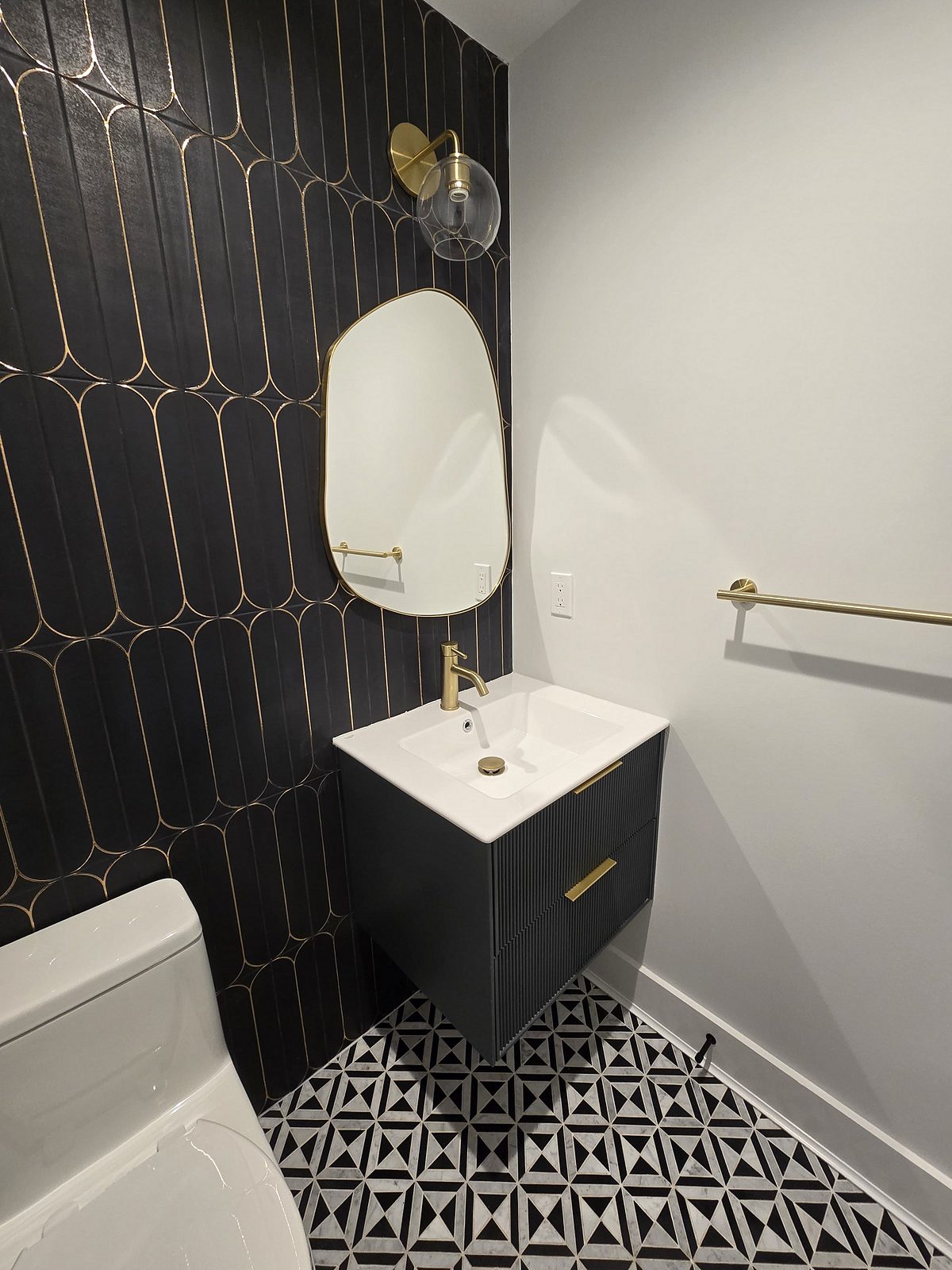 Powder room with a black floating vanity, brass faucet and gold-lined black tile