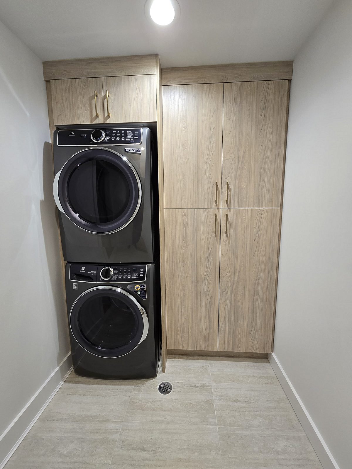 Laundry with a stacked washer and dryer in matching driftwood cabinets
