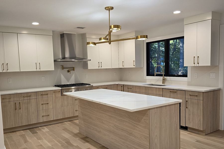 White and driftwood flat-panel kitchen with a marble-look quartz island, a brass linear chandelier and a stainless chimney hood