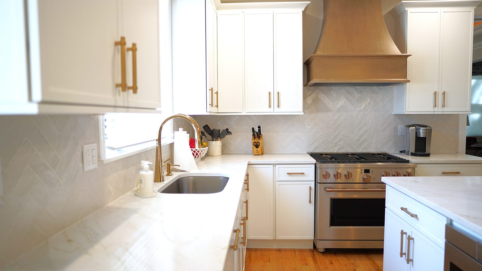 Pro-style range under the wood hood, with brass bar pulls and the herringbone backsplash